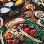 Top view of a vibrant assortment of fresh Asian vegetables and spices on a wooden table.